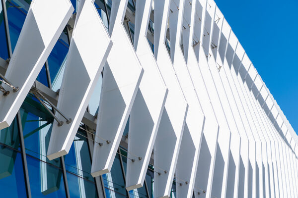 Modern building facade with large, white, angled panels casting shadows over glass windows