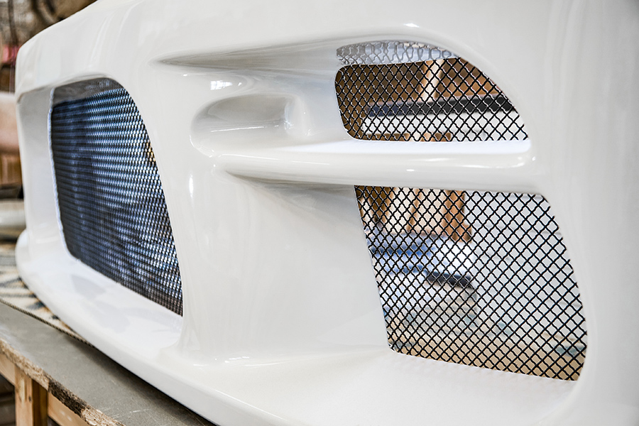 Close-up of a white car bumper with black mesh grille inserts, showing smooth, glossy surface and detailed vents. 