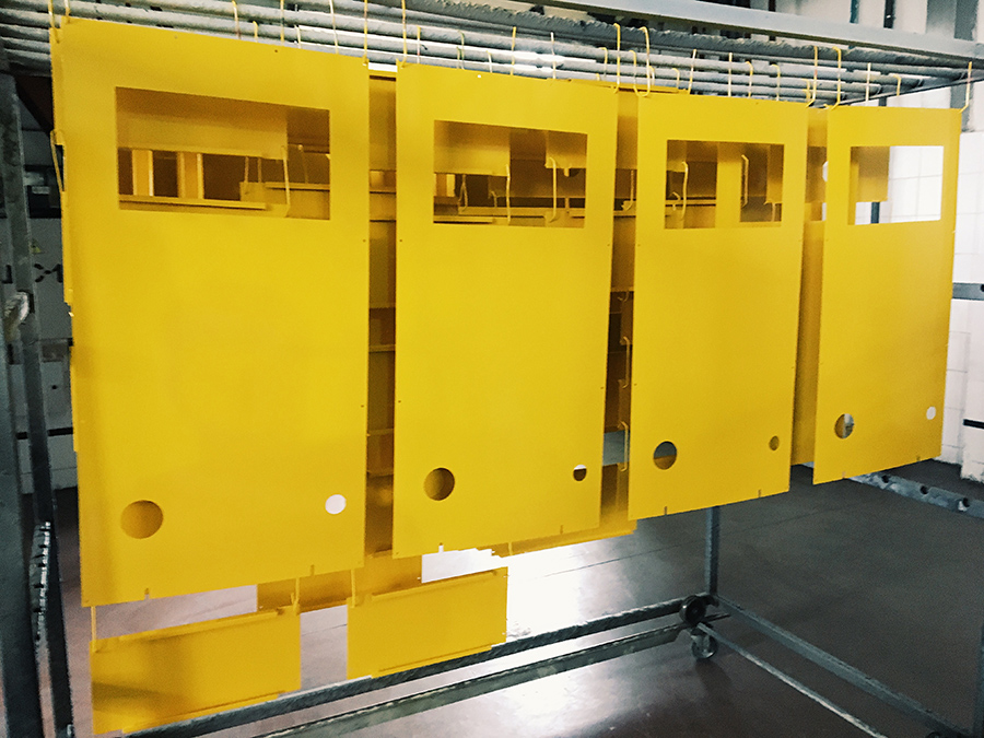 Four large yellow metal panels with cutouts are hanging vertically from hooks on a metal rack